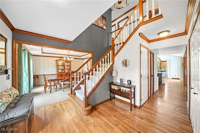 Staircase with ornamental molding, wallpapered walls, a textured ceiling, a chandelier, and wood finished floors