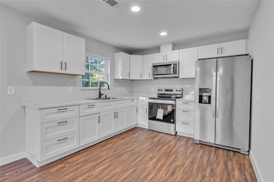 Kitchen with appliances with stainless steel finishes, white cabinetry, dark wood-style flooring, and recessed lighting