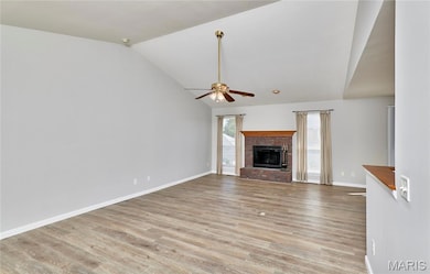 Unfurnished living room featuring lofted ceiling, a fireplace, light wood-style floors, and a ceiling fan