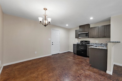 Kitchen featuring black range with electric stovetop, stainless steel microwave, dark brown cabinets, dark stone counters, and decorative light fixtures