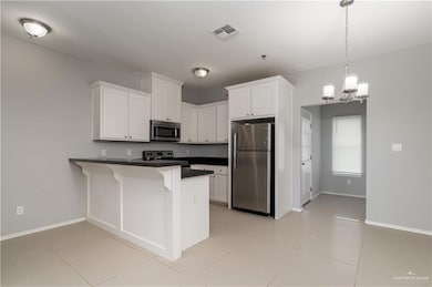 Kitchen featuring stainless steel appliances, a peninsula, dark countertops, and white cabinets