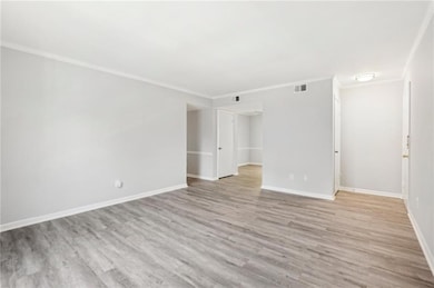 Empty room featuring crown molding, wood finished floors, and baseboards