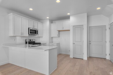 Kitchen with stainless steel appliances, baseboards, white cabinetry, and a peninsula
