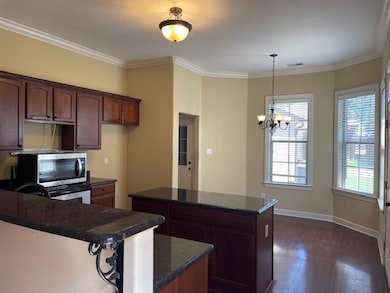 Kitchen with stainless steel microwave, dark wood-style flooring, a center island, a chandelier, and crown molding