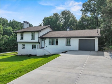 Tri-level home featuring driveway, a garage, a chimney, brick siding, and a front yard