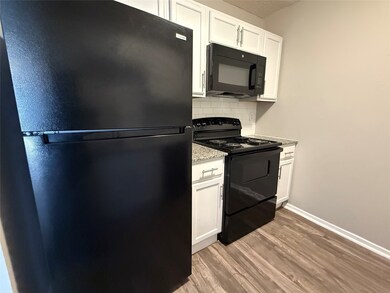 Kitchen with black appliances, white cabinets, light wood-type flooring, and tasteful backsplash
