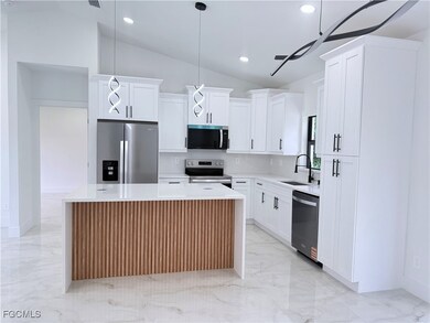 Kitchen featuring appliances with stainless steel finishes, vaulted ceiling, a kitchen island, light marble finish floors, and light stone counters