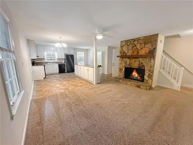 Unfurnished living room with light carpet, a chandelier, a fireplace, a ceiling fan, and stairs