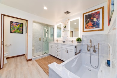 Bright, updated bath with marble walk-in shower, dual vanities with lighted mirrors, jetted soaking tub, and built-in storage. Includes a separate toilet room, a vanity makeup station, and integrated closet for added convenience.