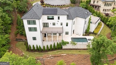 Rear view of property with stucco siding, roof mounted solar panels, a shingled roof, an outdoor pool, and fence
