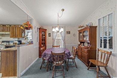 Dining space with wallpapered walls, a textured ceiling, a chandelier, wainscoting, and light carpet
