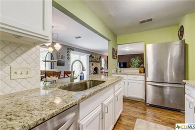 Kitchen featuring appliances with stainless steel finishes, white cabinets, light stone countertops, light wood-style floors, and a peninsula