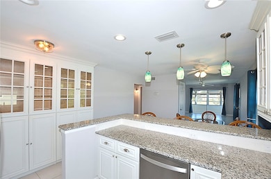 Kitchen with glass insert cabinets, light stone counters, white cabinetry, hanging light fixtures, and dishwasher