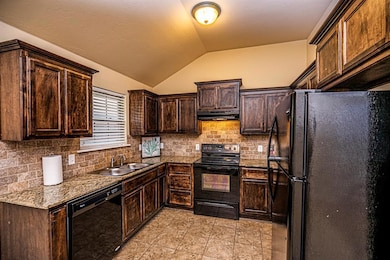 Kitchen featuring black appliances, under cabinet range hood, vaulted ceiling, dark brown cabinets, and tasteful backsplash