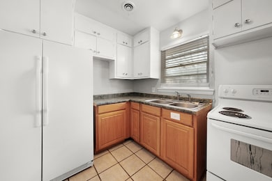 Kitchen featuring white appliances, dark countertops, light tile patterned flooring, brown cabinetry, and white cabinets