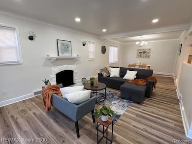 Living area featuring ornamental molding, a fireplace, wood finished floors, a chandelier, and recessed lighting