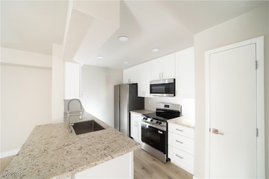 Kitchen featuring stainless steel appliances, white cabinets, light stone counters, light wood finished floors, and a peninsula