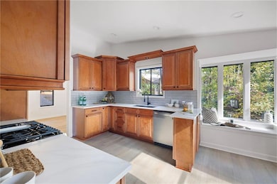 Kitchen featuring brown cabinetry, light wood-type flooring, stainless steel dishwasher, recessed lighting, and backsplash