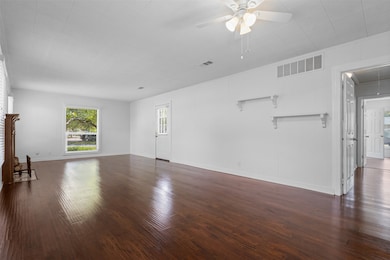 Unfurnished living room featuring attic access, dark wood-type flooring, and a ceiling fan