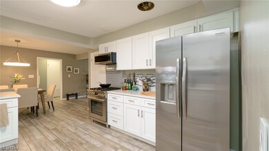 Kitchen featuring white cabinetry, light wood-type flooring, decorative light fixtures, appliances with stainless steel finishes, and backsplash