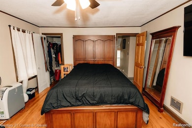 Bedroom featuring crown molding, a textured ceiling, light wood-type flooring, and a ceiling fan