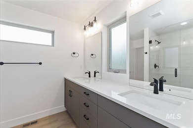 Full bath featuring double vanity, a shower stall, and light wood-style floors