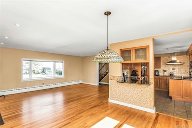 Kitchen featuring brown cabinetry, light wood-type flooring, backsplash, pendant lighting, and baseboard heating