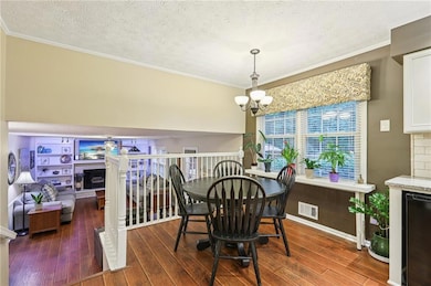 Dining space with hardwood / wood-style flooring, a chandelier, a textured ceiling, ornamental molding, and a fireplace with raised hearth