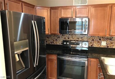 Kitchen with stainless steel appliances, brown cabinets, decorative backsplash, and dark stone countertops