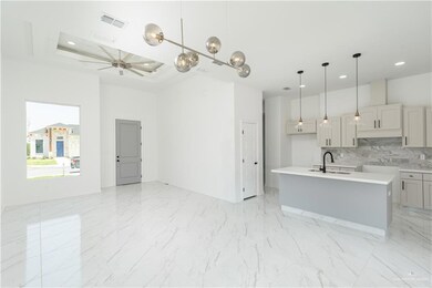 Kitchen with ceiling fan, an island with sink, decorative light fixtures, a raised ceiling, and sink