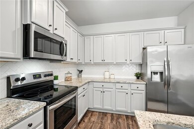 Kitchen with stainless steel appliances, dark wood-style flooring, backsplash, light stone counters, and white cabinets