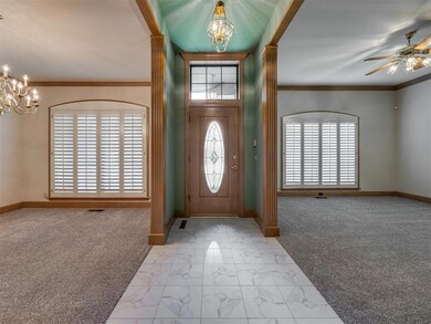 Carpeted entryway featuring a chandelier, baseboards, ceiling fan, crown molding, and ornate columns