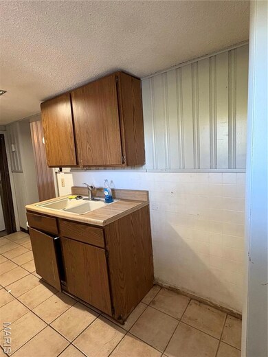 Kitchen with a textured ceiling, light countertops, light tile patterned floors, and brown cabinetry
