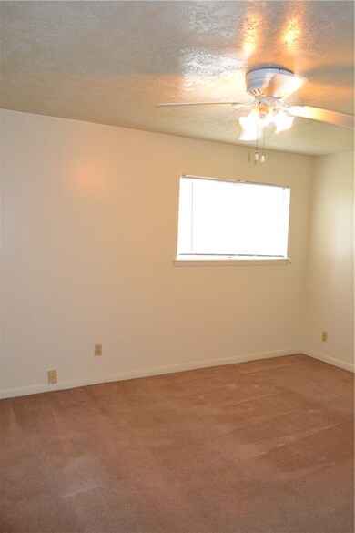 Empty room with light colored carpet, ceiling fan, a textured ceiling, and baseboards
