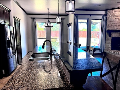 Kitchen featuring stainless steel fridge, a sink, crown molding, a kitchen island with sink, and dark stone counters