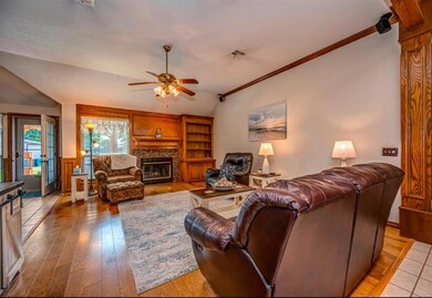 Living area featuring lofted ceiling, ceiling fan, crown molding, light wood finished floors, and a stone fireplace