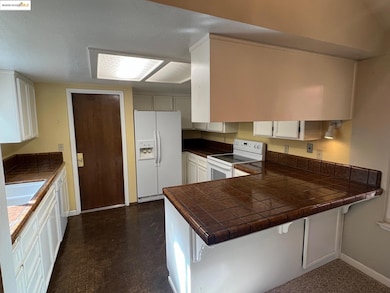 Kitchen with tile counters, white cabinetry, white appliances, a peninsula, and a textured ceiling