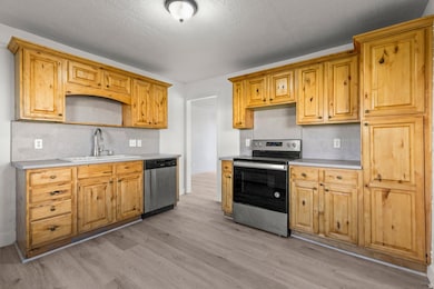 Kitchen with stainless steel appliances, light countertops, light wood-type flooring, and a textured ceiling