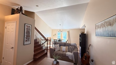 Living room featuring vaulted ceiling, dark wood-type flooring, a chandelier, stairway, and a textured ceiling