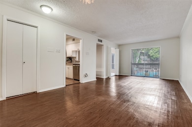 Unfurnished living room featuring crown molding, dark wood-style floors, and a textured ceiling