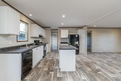 Kitchen featuring black appliances, dark countertops, a kitchen island, light wood-style flooring, and white cabinets