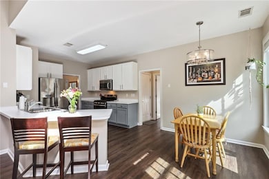 Kitchen with appliances with stainless steel finishes, white cabinets, dark wood-type flooring, a breakfast bar area, and gray cabinets