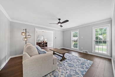 Living room with dark wood-type flooring, a ceiling fan, and crown molding