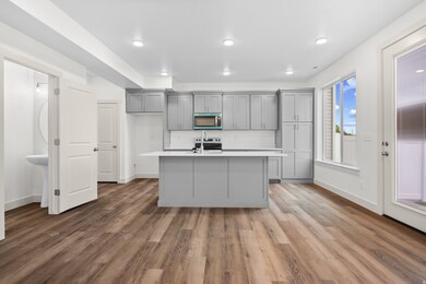 Kitchen with gray cabinetry, light countertops, light wood finished floors, stainless steel microwave, and a center island with sink