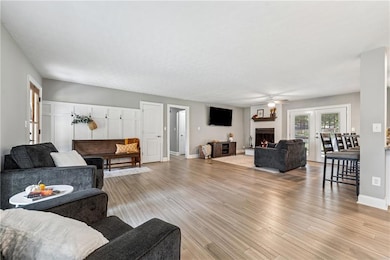 Living area with a lit fireplace, light wood-style floors, a ceiling fan, and french doors