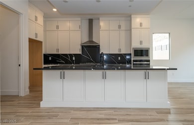 Kitchen featuring wall chimney exhaust hood, an island with sink, white cabinets, wood tiled floors, and tasteful backsplash