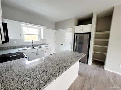Kitchen with freestanding refrigerator, light stone countertops, white cabinets, a sink, and light wood-style flooring