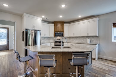 Kitchen featuring light stone counters, a kitchen island with sink, white cabinetry, tasteful backsplash, and a breakfast bar