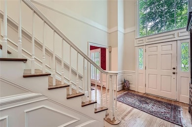 Foyer entrance featuring a towering ceiling, stairs, wood finished floors, a decorative wall, and a wainscoted wall
