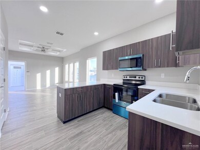 Kitchen with stainless steel microwave, range with electric cooktop, a sink, a peninsula, and light countertops